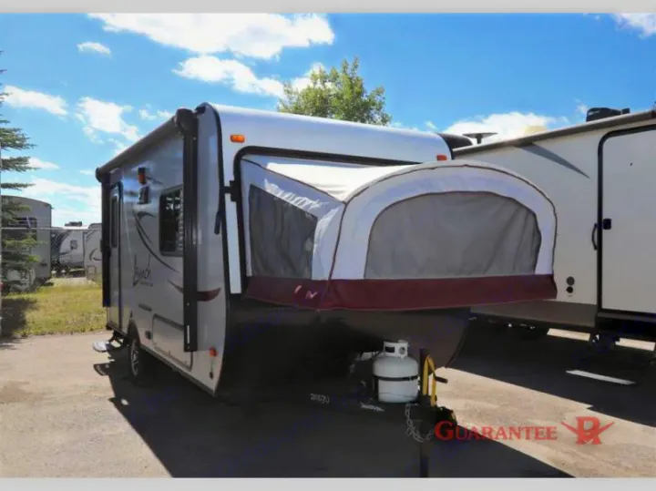 This white hybrid travel trailer, an ideal RV rental, features an expandable tent bed and front propane tank, parked outdoors.. Starcraft Launch 2016