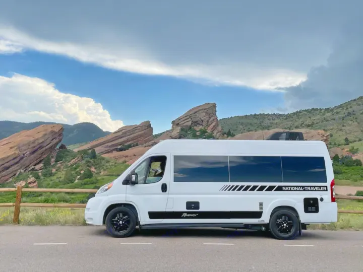 White National Traveler rv rental parked by impressive red rock formations and mountains under a cloudy sky.. Regency RV National Traveler 2019