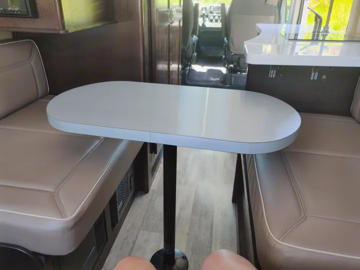 Inside an RV rental: a comfortable dinette with opposing benches, table, and compact kitchen with sink.. Regency RV National Traveler 2019