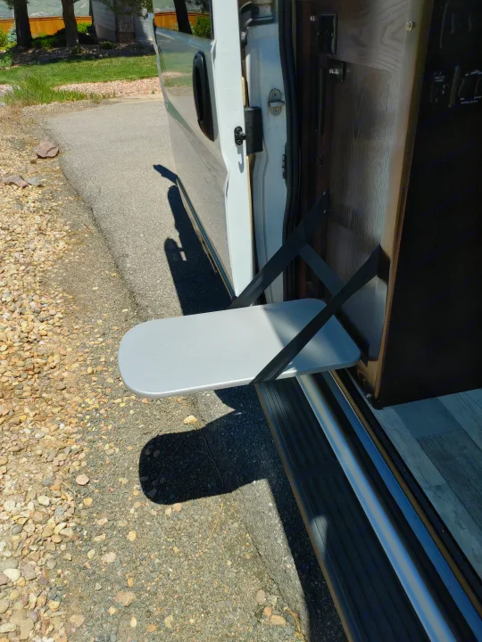 RV rental with a gray fold-out table, supported by black straps, extending from the open side door. Great for outdoor use.. Regency RV National Traveler 2019