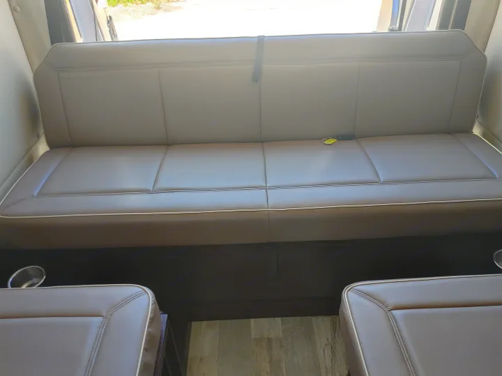 RV rental with comfortable light brown bench seating, white piping details, and convenient cup holders.. Regency RV National Traveler 2019