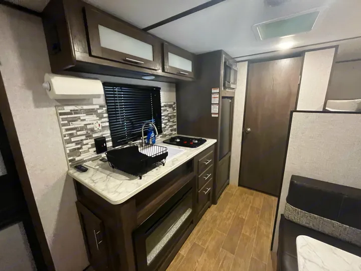 Functional RV rental kitchen and dinette area, showcasing compact design with a sink, stovetop, microwave, and ample storage.. Coleman CM17B21 2021