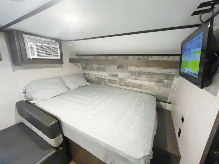 **RV rental**: A compact bedroom featuring a bed with gray linens, wall-mounted AC, and TV for a comfortable stay.. Coleman CM17B21 2021