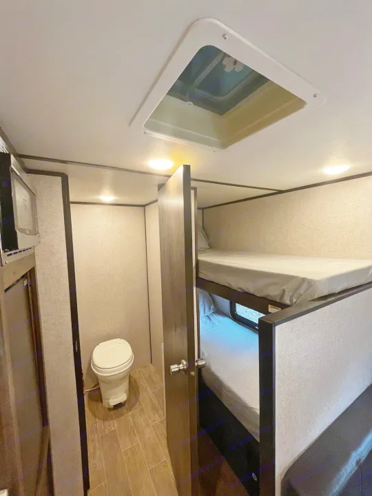 Inside an RV rental: compact bathroom with toilet, bunk beds, and ceiling vent for light.. Coleman CM17B21 2021