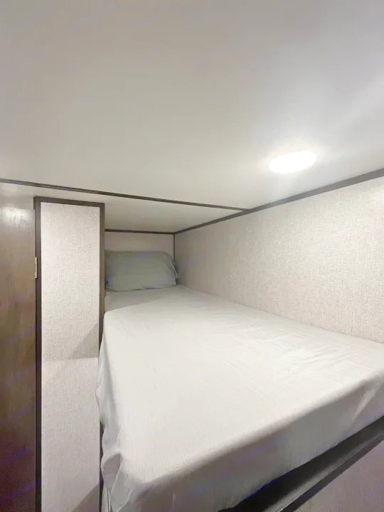 Cozy RV rental bunk bed featuring a grey bed, textured walls, and overhead light. Ideal compact sleeping space.. Coleman CM17B21 2021