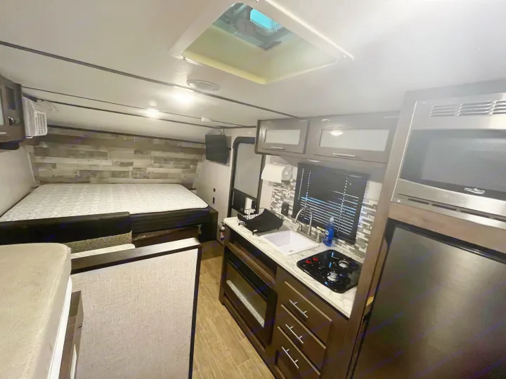 Spacious RV rental interior: kitchen with sink & stovetop, bed, microwave, and skylight.. Coleman CM17B21 2021