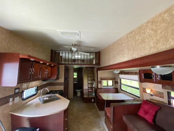 View inside an RV rental, featuring a functional kitchen, comfortable dining area, lounge seating, and an overhead loft with ladder.. Other Other 2009