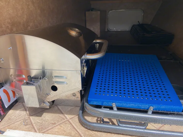 RV rental storage: A wet stainless steel grill and a blue perforated table are stored in the compartment, ready for camping.. Other Other 2009