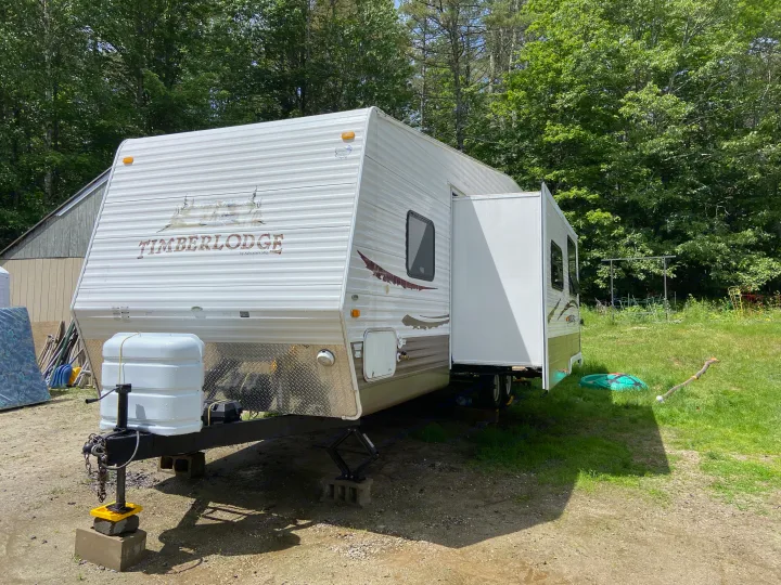 White Timberlodge travel trailer (an rv rental) with extended slide-out, parked on blocks in a wooded setting.. Other Other 2009