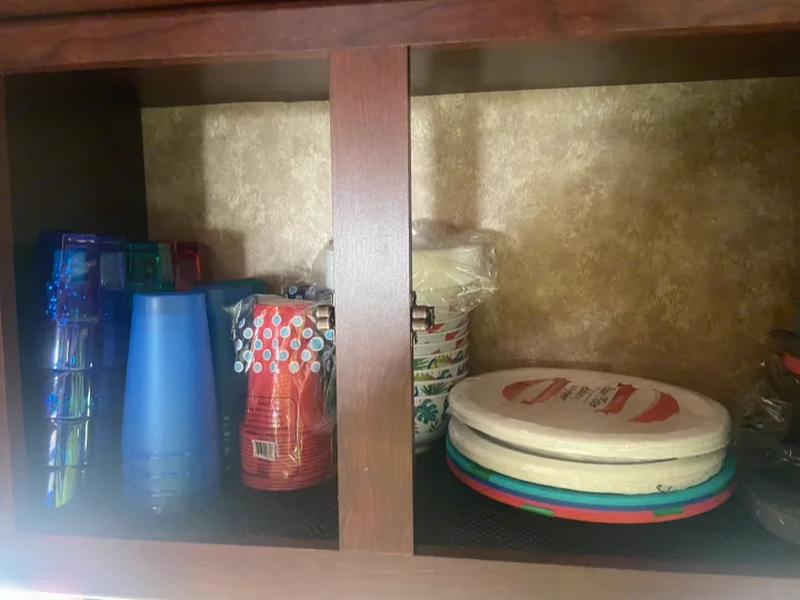 RV rental cabinet: organized plastic cups, paper plates, and bowls, including colorful and patterned designs. Travel essentials.. Other Other 2009