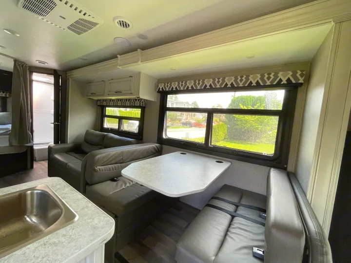 Bright RV rental interior showing a comfortable dinette, sofa, and small kitchen sink area with outdoor views.. Jayco Redhawk 2021