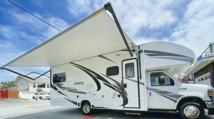 A white Jayco Redhawk Class C motorhome RV rental with its awning extended, parked on a sunny day.. Jayco Redhawk 2021