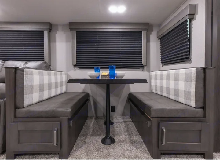 Cozy RV rental dinette features plaid benches, a table for meals, and integrated storage, ideal for road trips.. Grand Design Transcend 2020