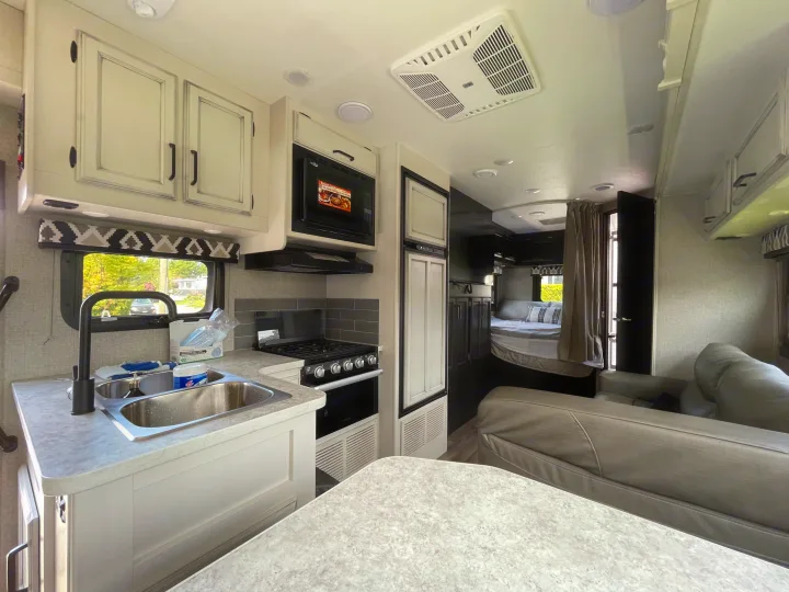 Spacious RV rental interior: modern kitchen with sink, stove, and microwave, opens to a cozy bedroom and living area.. Jayco Redhawk 2021