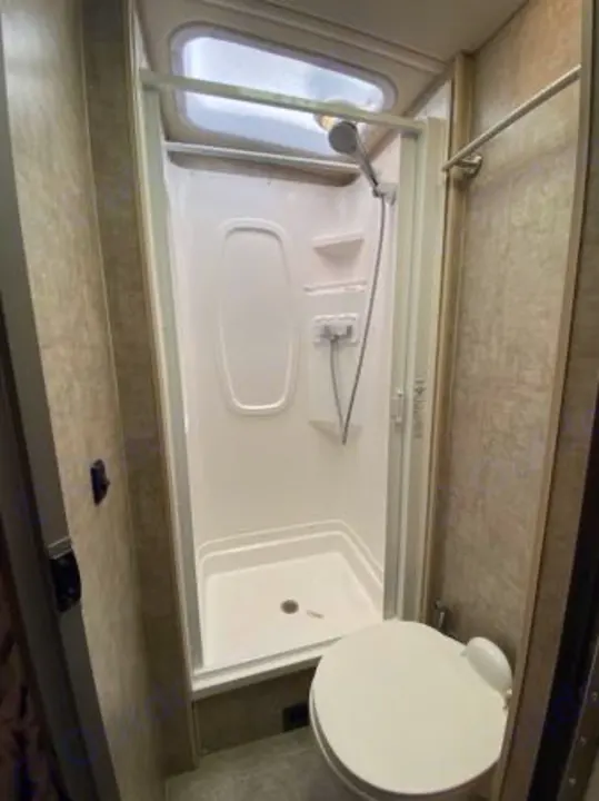Clean RV rental bathroom features a compact shower, toilet, and overhead skylight, maximizing space.. Itasca Navion 2015