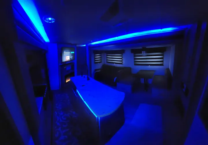 Modern RV rental interior with vibrant blue LED lighting, showing kitchen island, TV, and living space.. Forest River Cherokee Alpha Wolf 2021