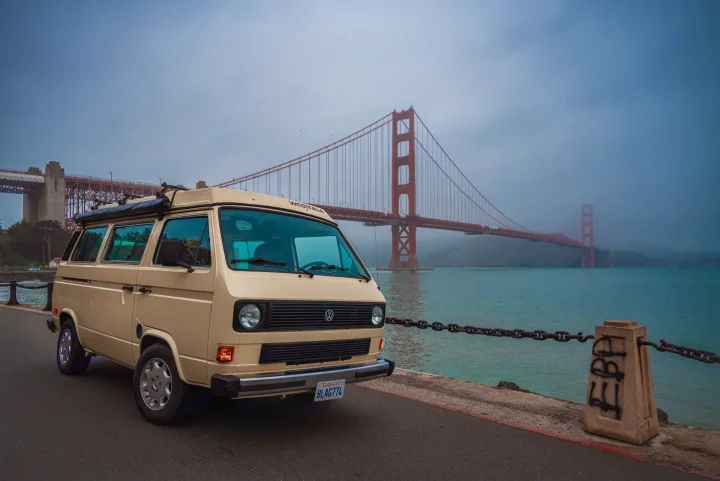 Explore San Francisco with an RV rental! A beige VW Westfalia parked by the Golden Gate Bridge, showcasing coastal travel.. Volkswagen Westfalia 1982