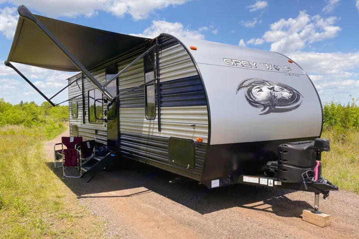 This Grey Wolf travel trailer, ideal for an RV rental getaway, is set up outdoors with its awning extended and chairs.. Forest River Cherokee Greywolf 2022