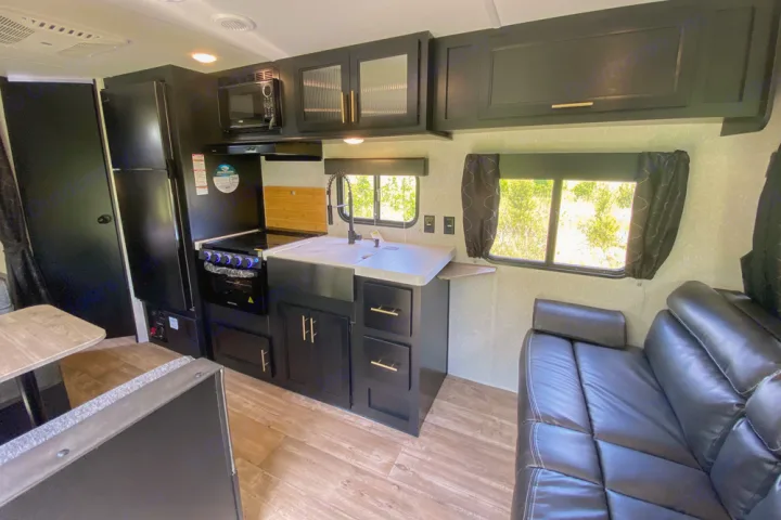 Spacious RV rental interior featuring a modern black kitchen, complete with sink, stove, and comfortable couch.. Forest River Cherokee Greywolf 2022