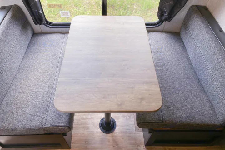 Clean RV rental dinette featuring a light wood table and gray upholstered booth seating with a window view, perfect for meals.. Forest River Cherokee Greywolf 2022