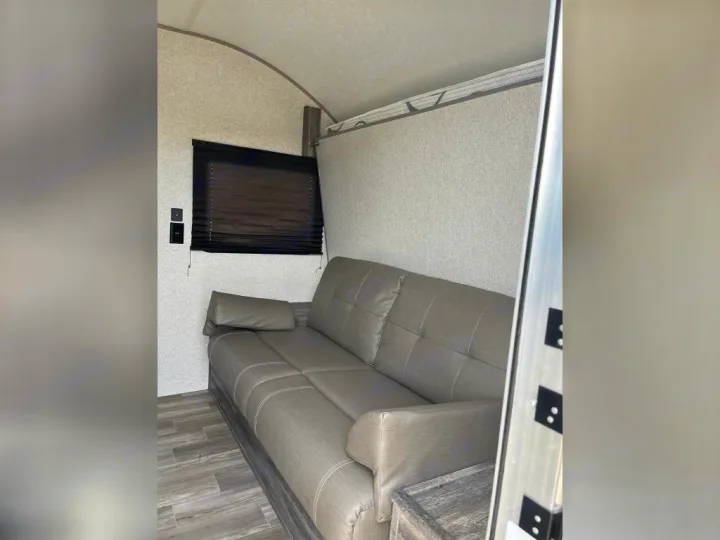 RV rental interior: Grey sofa, window with dark blind. A light panel above hints at a fold-down bed for flexible sleeping.. Forest River Wildwood FSX 2020