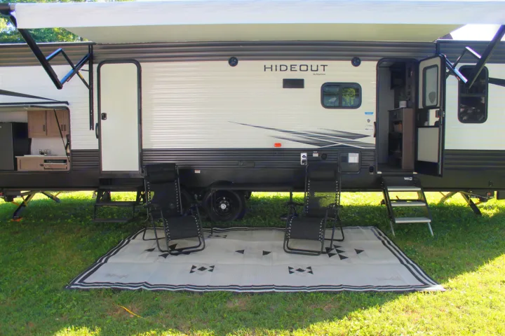This spacious RV rental offers an inviting outdoor living area: extended awning, outdoor kitchen, and patio with chairs on a mat.. Keystone RV Hideout 2021