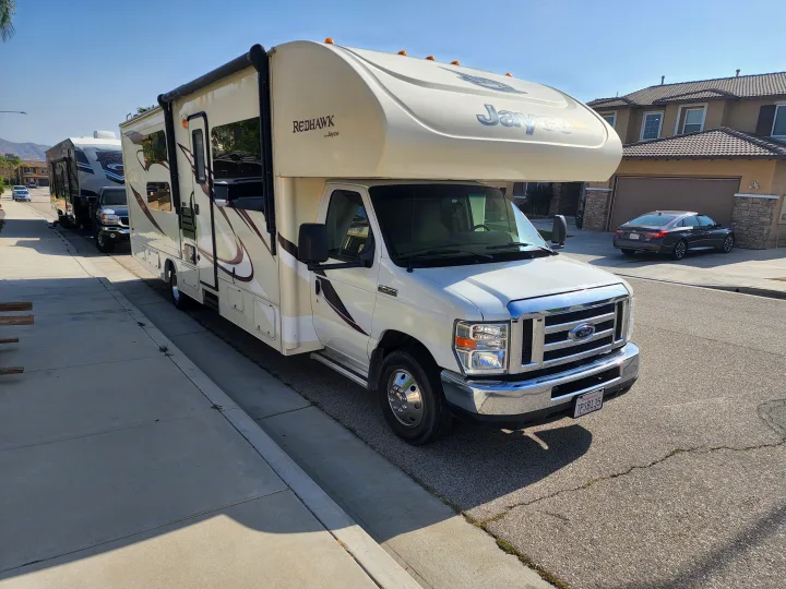 A white Jayco Redhawk Class C RV is parked on a sunny residential street, ideal for your next RV rental.. Jayco Redhawk 2016