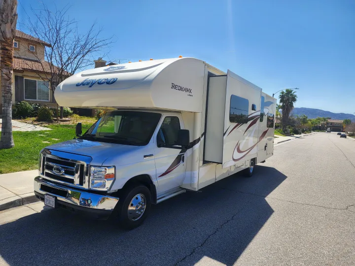 A white Jayco Redhawk RV, suitable for rv rental, is parked on a sunny street with its side slide-out extended.. Jayco Redhawk 2016