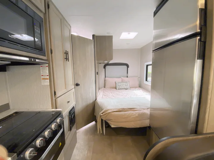 Inside this RV rental: a well-equipped kitchen area, comfortable bed with 'Happy Camper' pillow, and a shiny fridge.. Forest River Coachmen Cross Trail XL 2022