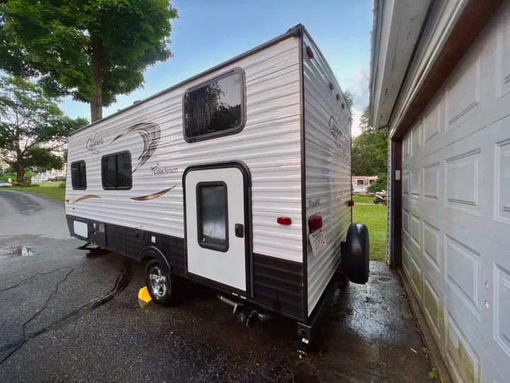 Side view of a white travel trailer RV rental, freshly washed & parked on a wet driveway next to a garage.. Coachmen Clipper 2016