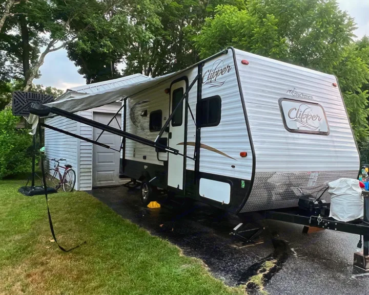 White & black Coachmen Clipper travel trailer with extended awning, parked on pavement by a shed. Perfect for your rv rental adventure!. Coachmen Clipper 2016