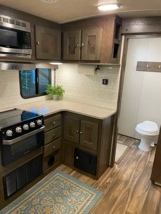 Inside an RV rental: modern kitchen with subway tile, oven, microwave, and adjacent compact bathroom.. Cruiser RV MPG Ultra Lite 2019