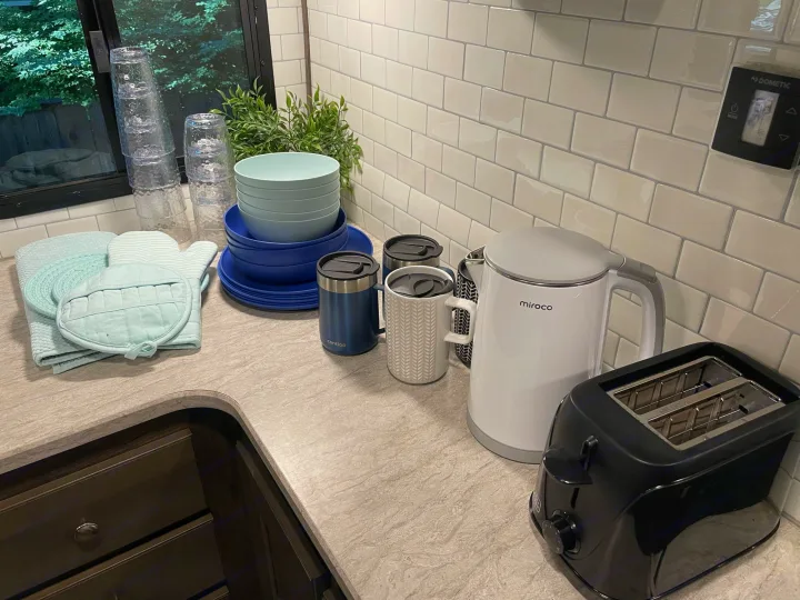 Compact rv rental kitchen essentials: kettle, toaster, dishes, & cups neatly arranged on the counter with a tiled backsplash.. Cruiser RV MPG Ultra Lite 2019