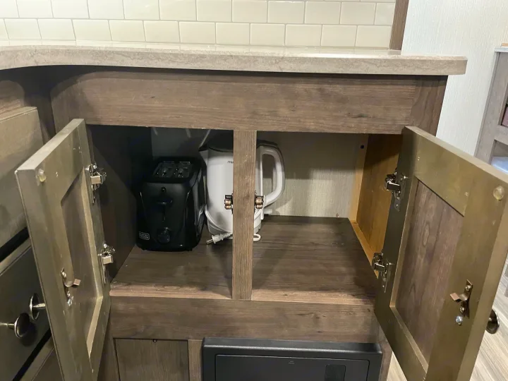 RV rental kitchen: Open cabinet with black toaster and white electric kettle. Countertop above, secure door latches visible.. Cruiser RV MPG Ultra Lite 2019
