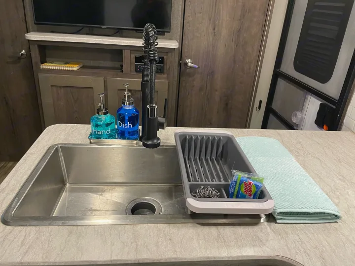 RV rental kitchen: Stainless steel sink, black faucet, hand/dish soaps, and a tidy drying station with scrubbers and mat.. Cruiser RV MPG Ultra Lite 2019