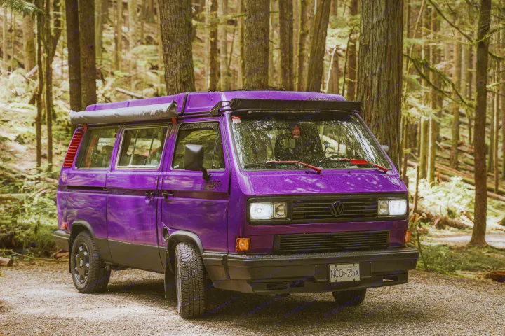 Vibrant purple VW camper van, an ideal RV rental, parked on a wet gravel forest road for wilderness adventures.. Volkswagen Vanagon 1991
