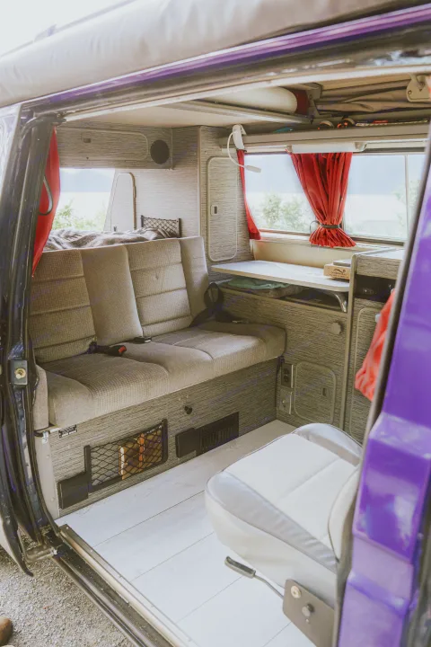 Inside a vibrant purple camper van, an RV rental with comfortable rear seating, a cozy bed, and a compact kitchen setup.. Volkswagen Vanagon 1991