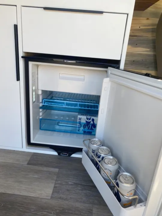 Compact RV rental fridge open, showing blue shelves and silver cans on the door. Ideal for beverages.. Ford Econoline E350 Extended 2004