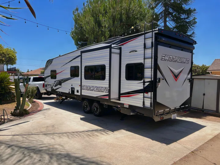 White SHOCKWAVE toy hauler RV rental parked on a sunny driveway. This large travel trailer has black & red accents.. Forest River Shockwave 2022
