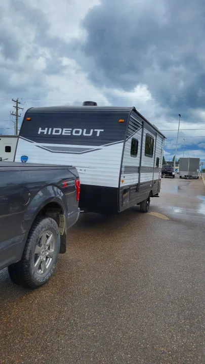 RV rental: Dark grey pickup truck towing a white & black 'Hideout' travel trailer on a wet lot under cloudy skies.. Keystone Hideout 2022