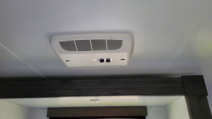 RV rental interior: Ceiling-mounted AC unit with fan controls for climate comfort, situated above a dark wooden beam.. Keystone Hideout 2022