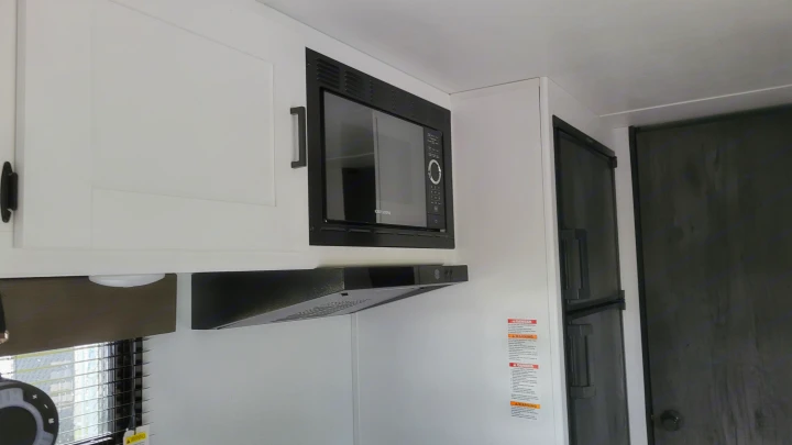 Inside an RV rental: a compact kitchen area with white cabinets, microwave, range hood, and refrigerator.. Keystone Hideout 2022
