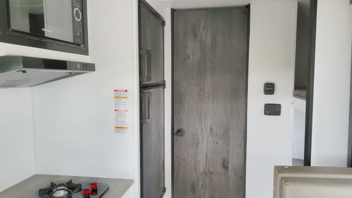 RV rental interior: kitchen with microwave, stove, and refrigerator, next to bunk beds and control panels.. Keystone Hideout 2022