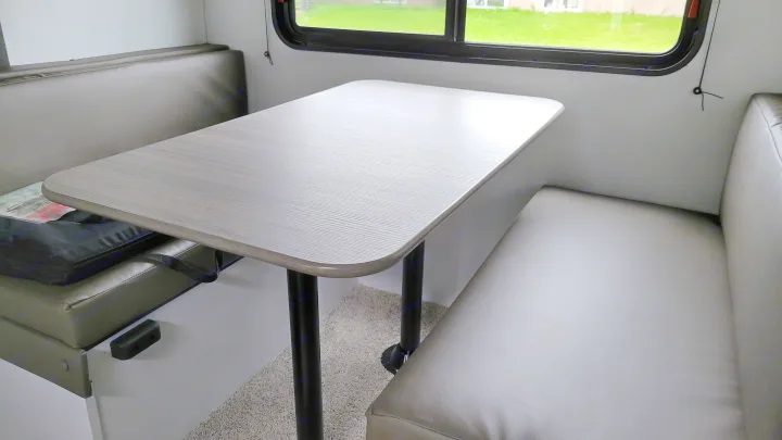 RV rental interior featuring a light gray wood-grain dinette table and comfortable upholstered benches by a window.. Keystone Hideout 2022