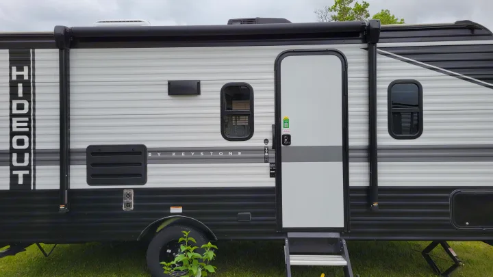 This white and black Hideout by Keystone travel trailer, ideal for rv rental, shows its entry door and windows.. Keystone Hideout 2022
