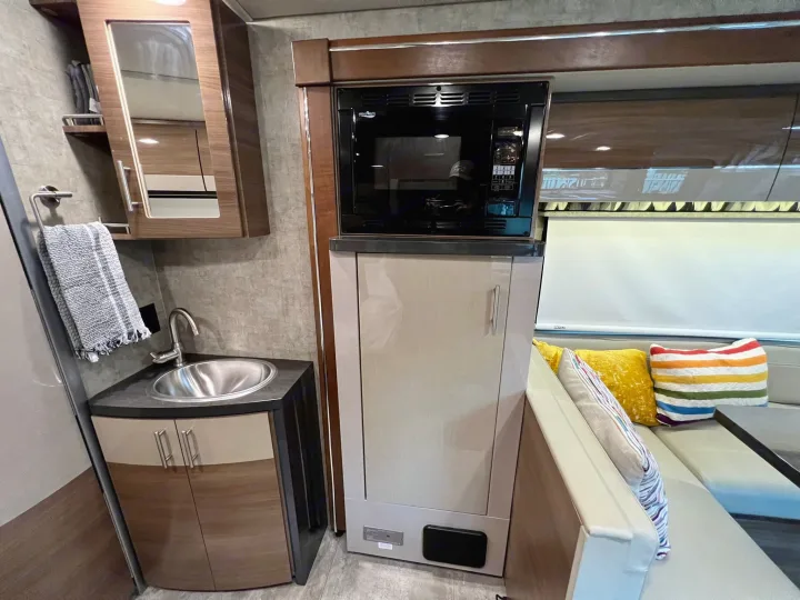 RV rental interior features a compact kitchenette with sink, microwave, cabinets, and an adjacent lounge seating area.. Itasca Navion 2015