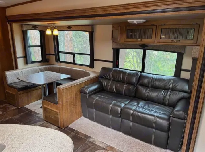 Inside a cozy RV rental: a bright living area with a U-shaped dinette and a comfortable black sofa.. Crossroads RV Rezerve 2016