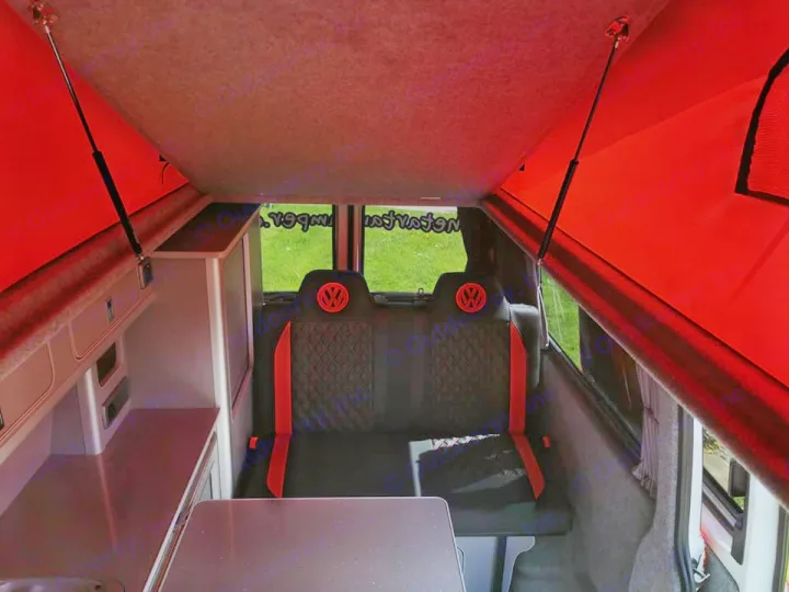 Inside a vibrant pop-top camper van with red accents, custom VW seating, and kitchen. Perfect for your next RV rental.. Volkswagen T6 Transporter LWB 2018