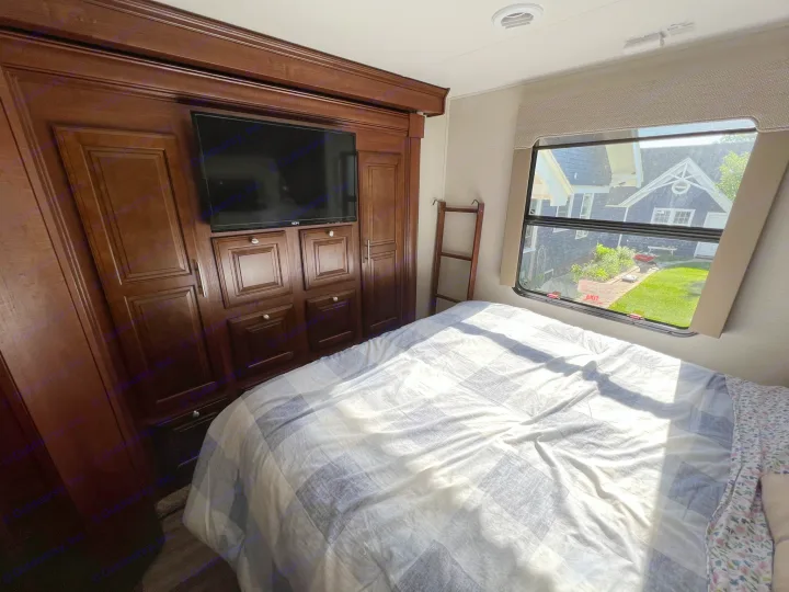 Cozy RV rental bedroom featuring a checkered bed, built-in TV cabinet, and window overlooking a green yard.. Georgetown 351 DS Bunkhouse 2017