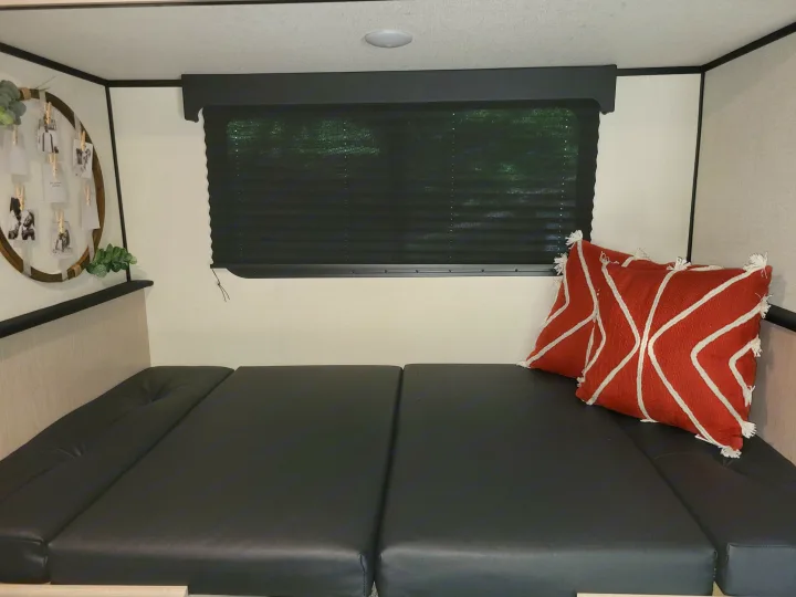 Cozy RV rental sleeping area with dark cushions, red accent pillows, a window blind, and personal decor.. Other Other 2022